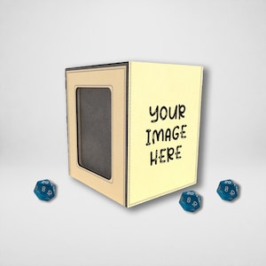 May include: A beige rectangular dice tower with a dark interior and a front-facing frame for customization. The side panel features the black text "YOUR image HERE". Three blue twenty-sided dice are positioned around the base of the tower.