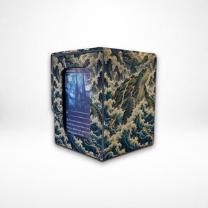 May include: A rectangular deck box featuring a sea turtle swimming through stylized blue ocean waves. The exterior has a textured finish with a central window displaying a blue-toned card with text and a stained-glass style illustration.