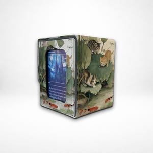May include: A rectangular deck box featuring a printed design of kittens playing among large green lotus leaves and orange koi fish in water. A clear window on the front displays a blue trading card with text and a stained glass illustration.