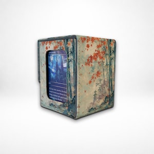 May include: A rectangular card storage box featuring a printed design of bamboo stalks and orange maple leaves. The front panel has a cutout window displaying a blue-toned trading card with text that includes the words Flooded Strand.