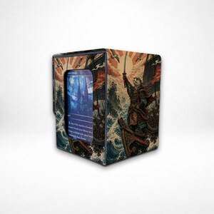 May include: A rectangular deck box for trading cards featuring a printed illustration of an otter samurai standing on a boat amidst turbulent waves. The box has a clear window on the front displaying a blue card with stained glass imagery.