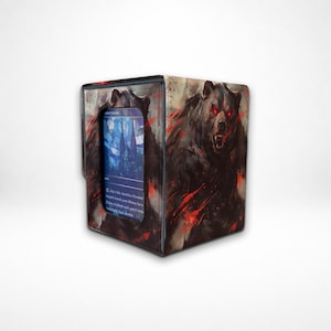 Op de afbeelding: Een rechthoekige deckbox voor ruilkaarten met een illustratie van een donkere, agressieve beer met gloeiende rode ogen en rode spetters. Een doorzichtig venster aan de voorzijde toont een blauwe kaart met tekst en een gebouwafbeelding.