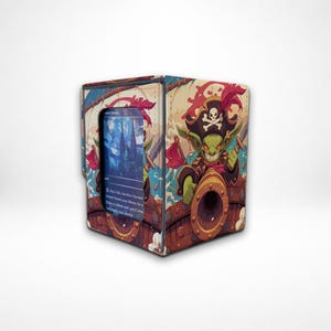 May include: A rectangular card storage box featuring a colorful illustration of a green goblin pirate wearing a skull and crossbones hat, positioned behind a cannon on a ship deck. A clear window displays a blue trading card with printed text.