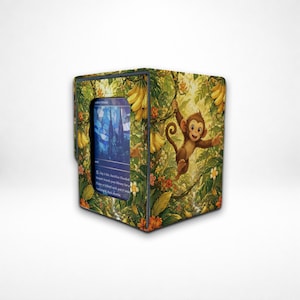 May include: A rectangular card storage box featuring a vibrant jungle scene with green foliage, yellow bananas, and a brown monkey. A rectangular window on the front displays a blue trading card with text that reads, Pay 1 life, Sacrifice Flooded Strand: Search your library for a Plains or Island card, put it into battlefield, then shuffle.