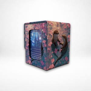 Puede incluir: Una taza de cerámica blanca con un asa negra y el texto "But First, Coffee" en negrita negra. La taza se encuentra sobre un fondo borroso, sugiriendo un ambiente acogedor.