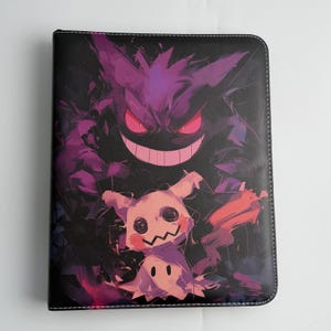 Peut inclure: Un classeur rectangulaire noir orné d'une impression graphique vibrante représentant un grand Gengar violet aux yeux rouges brillants et au large sourire, placé au-dessus d'un Mimikyu rose pâle aux yeux en spirale et à la bouche en zigzag.