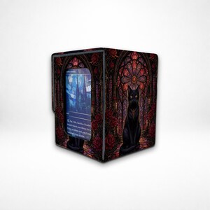 May include: A rectangular card storage box featuring a black cat sitting before a stained-glass window with red roses. The box displays a visible trading card with blue and white artwork and text, including the phrase Pay 1 life, Sacrifice Flooded Strand.