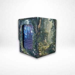 Peut inclure: Une boîte de jeu rectangulaire ornée d'une scène de forêt imprimée avec des arbres verts, du feuillage et de petits papillons blancs. Une fenêtre centrale rectangulaire affiche une carte à collectionner avec des motifs en vitrail bleu et violet.