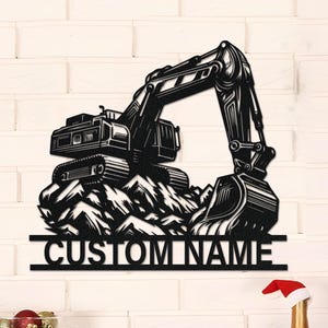 May include: Black metal excavator wall art with the text "CUSTOM NAME". The excavator is depicted on a rocky terrain. The art is mounted on a white brick wall, with holiday decorations in the foreground.