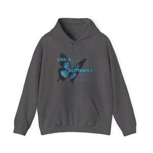 Könnte beinhalten: Ein anthrazitfarbener Kapuzenpullover mit einem blauen Schmetterlingsmotiv und dem Text "LIKE A BUTTERFLY" in hellblauer Schrift. Der Kapuzenpullover hat eine Vordertasche und eine Kapuze mit Kordelzug.