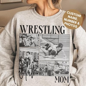Pode incluir: Uma camisola cinzenta clara de gola redonda com a palavra WRESTLING em preto, uma colagem de quatro fotografias de luta a preto e branco, o nome Arthur em cursivo, a palavra MOM e um emblema circular com CUSTOM NAME, NUMBER & PHOTOS.