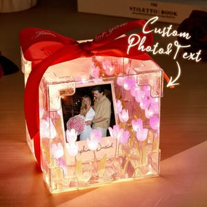 May include: A clear, cube-shaped photo frame with a red ribbon and the words "for you." The frame contains a photo of a couple and is decorated with pink flower lights. The text "Custom Photo & Text" is also visible.