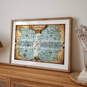 Op de afbeelding: Een ingelijste kaart in vintage-stijl met een lichtblauwe oceaan en bruine landmassa's. De kaart is gelabeld met kompasrichtingen en heeft decoratief krulwerk. De houten lijst complementeert de antieke esthetiek, geschikt voor woondecoratie.