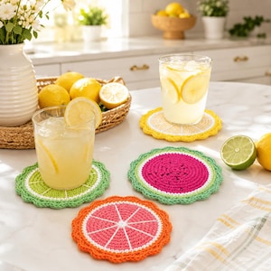 May include: A set of three round, crocheted drink coasters featuring fruit slice designs. One coaster is green with a lime pattern, one is pink with a watermelon pattern, and one is orange with a grapefruit pattern. Each has a scalloped edge.
