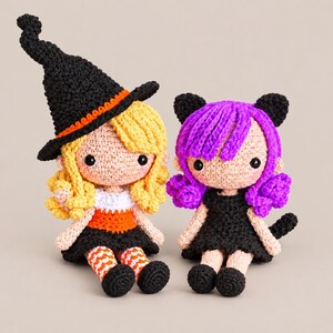 May include: Two handmade crochet dolls. The left doll has blonde hair, a black witch hat with an orange band, a white and orange top, a black skirt, and orange and white striped leggings. The right doll has purple hair, cat ears, and a black dress.