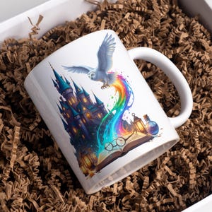Puede incluir: Taza de cerámica blanca con una ilustración de fantasía. Un búho blanco vuela sobre un castillo, con un arcoíris que emana de él. También se representan un libro abierto, gafas y botellas de pociones.
