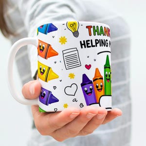 May include: White ceramic mug with a colorful crayon design and the words "Thank you for helping me grow." The mug features smiling crayon illustrations, hearts, and a lightbulb.