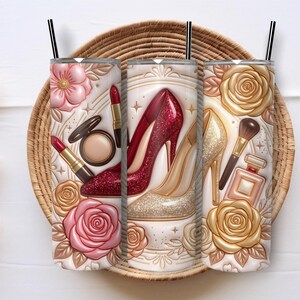 May include: Three white insulated tumblers with black straws, featuring a design of high heels, makeup, and roses. The design includes red and gold accents, with a decorative floral and makeup theme.
