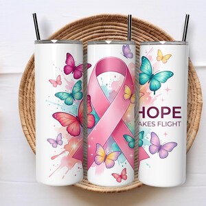 May include: White tumbler with a pink ribbon and colorful butterflies. The tumbler has the words "HOPE takes flight" printed on it. The design includes pink, teal, purple, and yellow butterflies. The tumbler has a black straw.