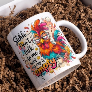 May include: White ceramic coffee mug with a colorful rooster illustration wearing glasses. The mug has the text "Shhh... Don't talk to me until my cup is empty" in black and pink. The mug is in a gift box with brown paper.