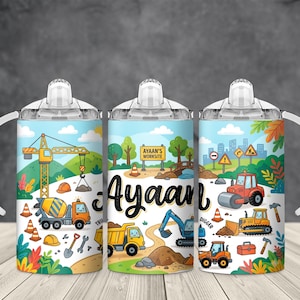 May include: Three sippy cups with construction-themed illustrations. Each cup features a different construction vehicle, including a crane, cement truck, and bulldozer. The name "Ayaan" is prominently displayed on the center cup. The cups have white handles and lids.