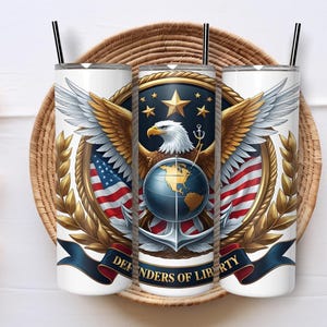 May include: Three white insulated tumblers with black straws, featuring a patriotic design. The design includes an eagle, American flags, a globe, and the text "Defenders of Liberty" on a navy blue banner. The tumblers are set on a woven tray.