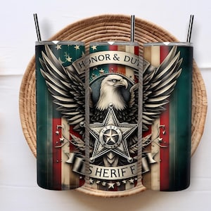 Pode incluir: Três copos de aço inoxidável com canudos pretos, com um design patriótico. O design inclui uma águia, asas, uma estrela e as palavras "Honor & Duty Sheriff" em um fundo vermelho, branco e azul.