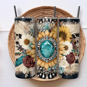 May include: Three stainless steel tumblers with black straws, each adorned with a floral design. The designs feature sunflowers, daisies, and a large turquoise gem. The tumblers rest on a woven tray.