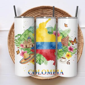 May include: Three white insulated tumblers with black straws, featuring watercolour designs of Colombia. The designs include the Colombian flag, landmarks, flowers, butterflies, and the word "COLOMBIA". The tumblers are set on a woven tray.