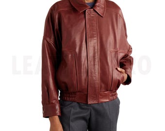 May include: A burgundy leather jacket with a collared neckline, two front pockets, and a ribbed hem. The jacket has a buttoned cuff and a relaxed fit. The model is wearing gray pants and a blue shirt.
