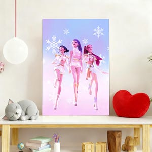 May include: A digital art print featuring three stylized female figures in white outfits with gold accents, set against a pastel blue and pink background with snowflake details. The artwork is displayed on a white table.