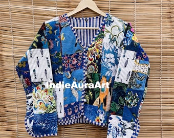 May include: A patchwork jacket with a V-neck design, featuring a variety of blue, white, and floral patterns. The jacket is displayed on a wooden hanger against a bamboo blind backdrop. The text "IndieAuraArt" is visible on the jacket.