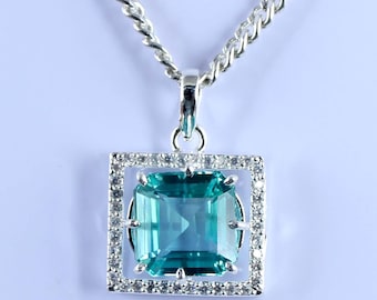 Könnte beinhalten: Silberkette mit quadratischem Anhänger. Der Anhänger hat einen großen, rechteckigen, teal-farbenen Edelstein, der von kleinen, klaren Edelsteinen umrahmt ist. Die Kette ist im Silber-Glieder-Stil gehalten. Der Edelstein misst ca. 2 cm.