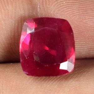 Op de afbeelding: Een gefacetteerde robijn edelsteen met kussensnede. De edelsteen heeft een diepe, verzadigde rode kleur met een hoge mate van helderheid. De slijping van de steen laat licht reflecteren, waardoor een briljant uiterlijk ontstaat. De robijn is een populaire keuze voor sieraden.