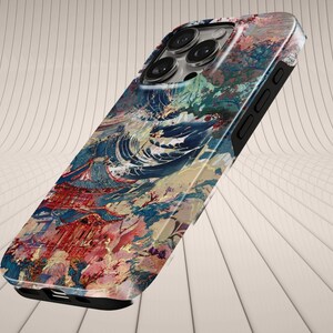 May include: A phone case featuring a colorful Japanese-inspired design. The case showcases a vibrant print of a wave, a red building, and floral elements. The case has a black border and a camera cutout.