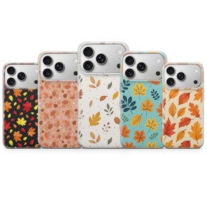 Könnte beinhalten: Fünf Smartphone-Hüllen mit verschiedenen Herbstblattmustern. Die Designs zeigen rote, orange und gelbe Blätter auf schwarzem, pfirsichfarbenem, weißem, blaugrünem und cremefarbenem Hintergrund. Jede Hülle hat einen Ausschnitt für drei Linsen.
