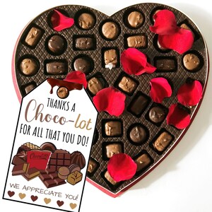 May include: A heart-shaped box filled with assorted chocolates, decorated with red rose petals. A tag attached to the box reads "Thanks a Choco-lot for all that you do!" with a chocolate bar illustration and the text "We appreciate you!"