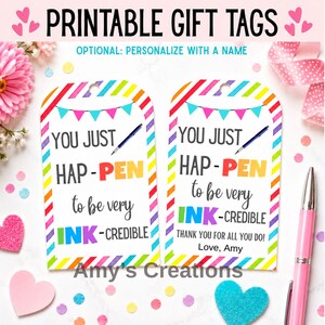 Op de afbeelding: Twee rechthoekige cadeaulabels met afgeronde bovenkanten en regenbooggestreepte randen. De tekst luidt: YOU JUST HAP-PEN to be very INK-CREDIBLE. Eén label bevat: THANK YOU FOR ALL YOU DO! Love, Amy. Het ontwerp toont een blauwe pen en vlaggetjes.