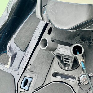 Puede incluir: Primer plano del interior de un barco con un asiento gris y un soporte para ca&ntilde;as de pescar. El interior del barco presenta una combinaci&oacute;n de colores negro y gris con un acento azul. Una ca&ntilde;a de pescar est&aacute; insertada en el soporte.