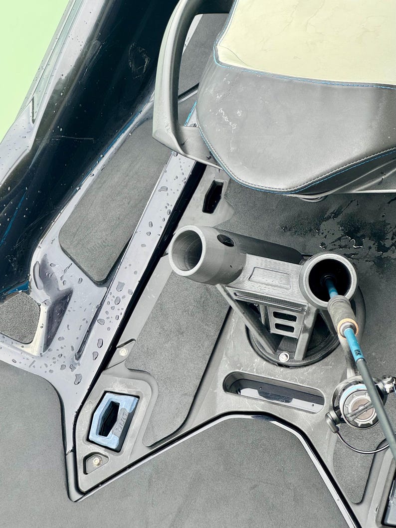 Puede incluir: Primer plano del interior de un barco con un asiento gris y un soporte para ca&ntilde;as de pescar. El interior del barco presenta una combinaci&oacute;n de colores negro y gris con un acento azul. Una ca&ntilde;a de pescar est&aacute; insertada en el soporte.