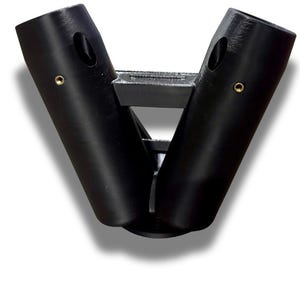 Puede incluir: Un objeto negro en forma de V con dos brazos cil&iacute;ndricos conectados por un soporte central. Cada brazo tiene una abertura ovalada y un peque&ntilde;o detalle circular de color dorado. El objeto parece estar hecho de un material mate.