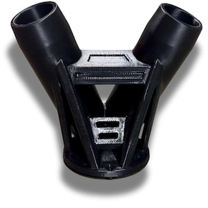 Puede incluir: Un objeto de pl&aacute;stico negro en forma de Y, con dos aberturas cil&iacute;ndricas en la parte superior y una base rectangular. El dise&ntilde;o es geom&eacute;trico, con soportes angulares y una caracter&iacute;stica rectangular central.