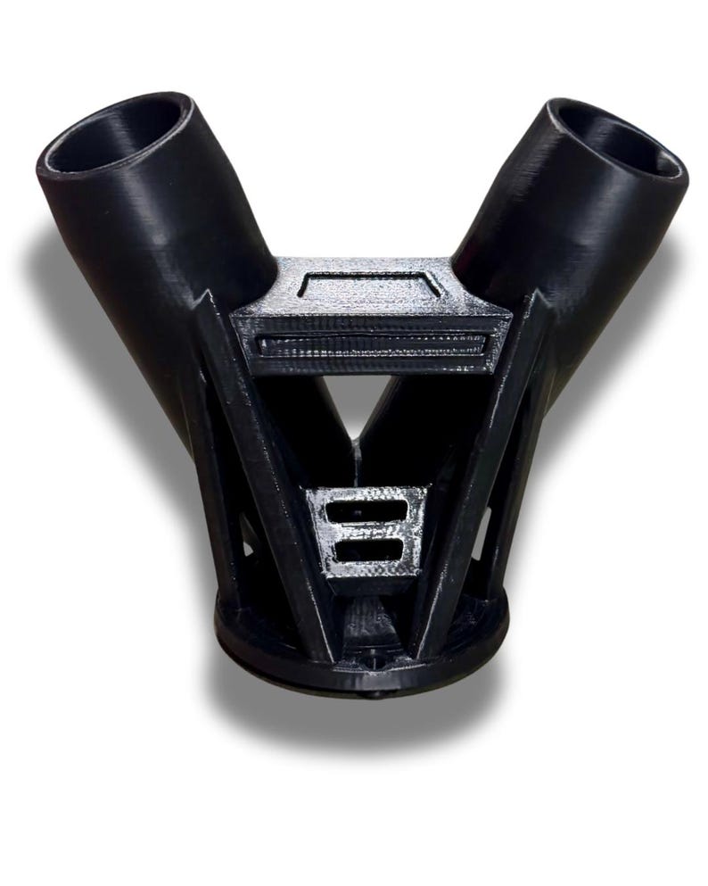 Puede incluir: Un objeto de pl&aacute;stico negro en forma de Y, con dos aberturas cil&iacute;ndricas en la parte superior y una base rectangular. El dise&ntilde;o es geom&eacute;trico, con soportes angulares y una caracter&iacute;stica rectangular central.