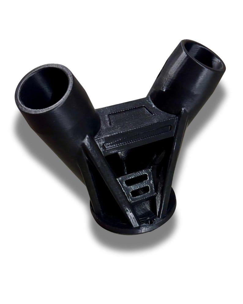Puede incluir: Un conector de pl&aacute;stico negro en forma de Y con dos aberturas cil&iacute;ndricas anguladas y una estructura de soporte central. El conector tiene una superficie texturizada y est&aacute; dise&ntilde;ado para unir tubos o tuber&iacute;as. La base es circular.