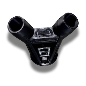Puede incluir: Un conector de pl&aacute;stico negro en forma de Y con dos aberturas cil&iacute;ndricas anguladas desde una base central geom&eacute;trica. El objeto est&aacute; impreso en 3D, con l&iacute;neas de capa visibles y un acabado mate. El dise&ntilde;o sugiere un componente funcional, posiblemente industrial.