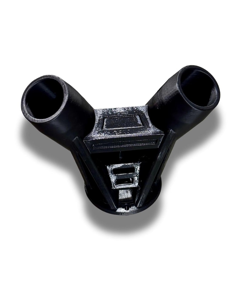 Puede incluir: Un conector de pl&aacute;stico negro en forma de Y con dos aberturas cil&iacute;ndricas anguladas desde una base central geom&eacute;trica. El objeto est&aacute; impreso en 3D, con l&iacute;neas de capa visibles y un acabado mate. El dise&ntilde;o sugiere un componente funcional, posiblemente industrial.