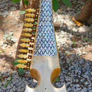 May include: A stringed musical instrument with a long neck inlaid with iridescent mother-of-pearl teardrop shapes. The body is light-colored wood with a smooth, rounded base and multiple yellow tuning pegs along the side with black and red accents.