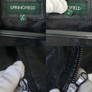 May include: A black leather jacket featuring a green brand label with the text SPRINGFIELD, EUR M, T-3, and MEX 38. The jacket includes a metal zipper pull engraved with the text LAMPO and MADE IN ITALY, showcasing the brand details and hardware.
