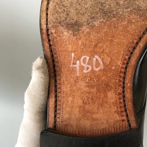 May include: Close-up of the sole of a black leather shoe. The sole is brown with visible wear and tear. The number "480" is written in white. The words "Goodyear Welted" are also visible.