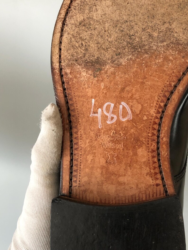 May include: Close-up of the sole of a black leather shoe. The sole is brown with visible wear and tear. The number "480" is written in white. The words "Goodyear Welted" are also visible.